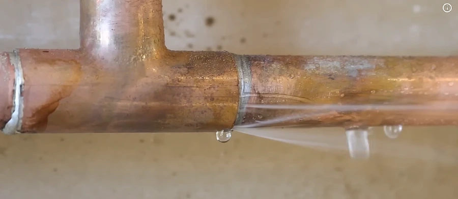 Hands setting a new PVC tee fitting in a trench during drain repair
