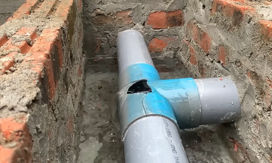 Broken PVC drain pipe with a crack in an underground trench, before repair